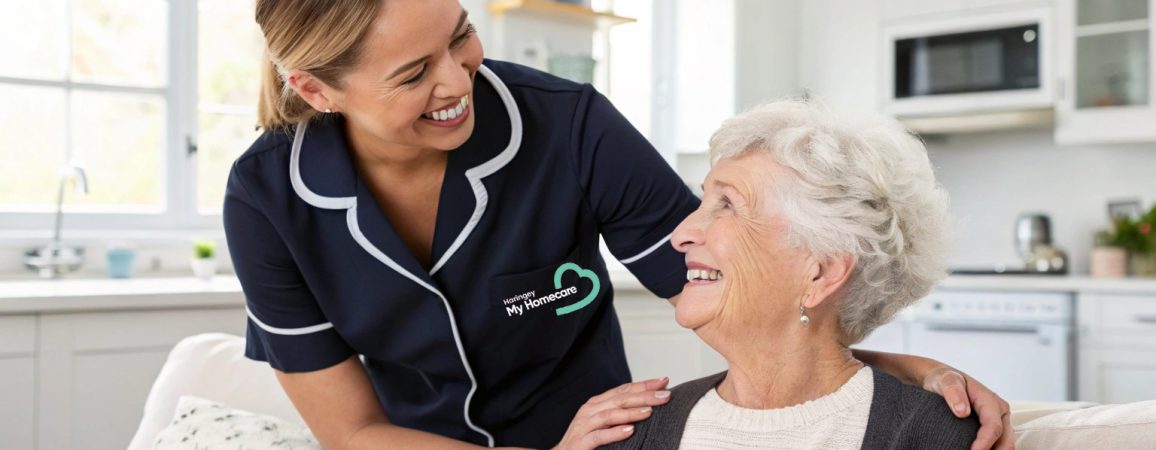Caregiver in My Homecare uniform smiling warmly at an elderly woman in a bright, modern kitchen setting.