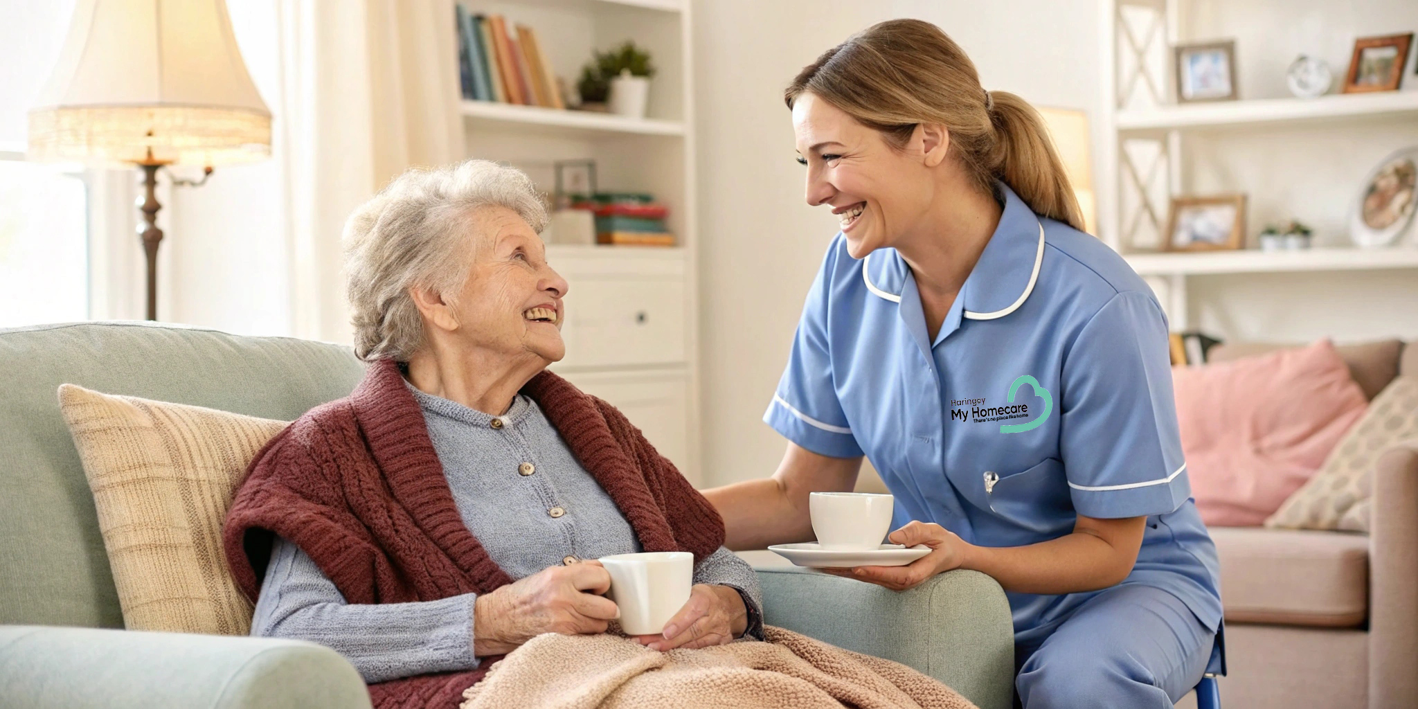 Elderly woman smiles at caregiver offering tea in a cozy home, both enjoying a warm and caring moment.